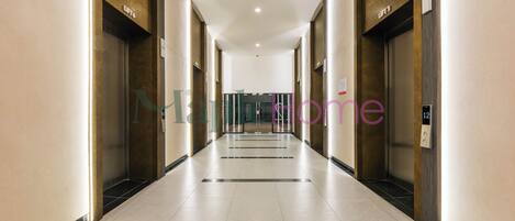 A long, narrow hallway with a tiled floor and walls, flanked by elevators and doors.