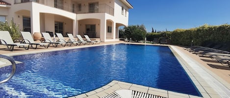A swimming pool with lounge chairs and a building with balconies.