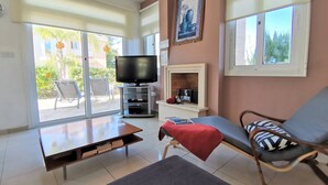 A living room with a TV, a fireplace, a sofa, and a dining table. - Aurora Villa Protaras - Private Pool Wifi (Paralimni)