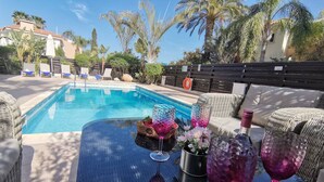 A poolside area with a clear blue pool, wicker furniture, and a table with decorative items. - Aurora Villa Protaras - Private Pool Wifi (Paralimni)