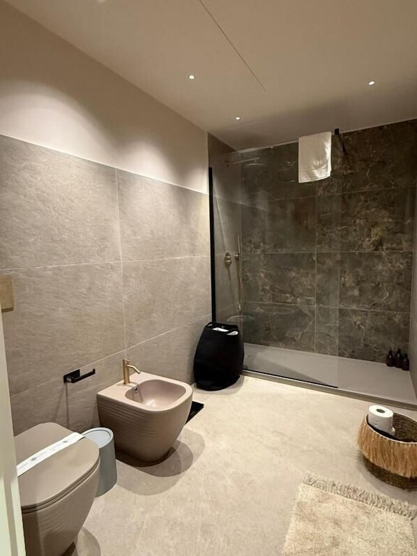A modern bathroom with a bidet, toilet, and a glass-enclosed shower area.