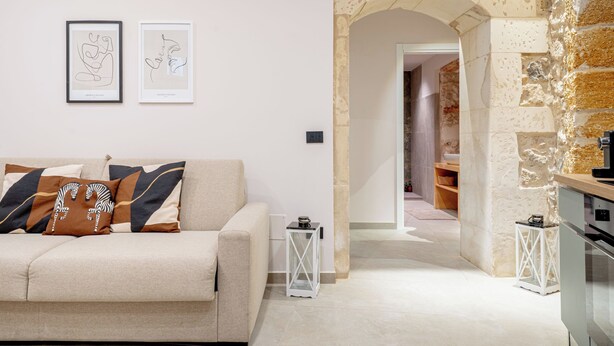Un salon moderne avec un canapé, deux œuvres d’art encadrées et une arche en pierre menant à une autre pièce.