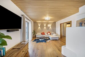 Een moderne woonkamer met een flatscreen televisie, een houten salontafel, een bank met kussens, een kamerbreed tapijt en een plafondlamp.