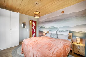 Een slaapkamer met een bed, een nachtkastje, een wandlamp, een ronde spiegel en een deur met een rood rond ontwerp.