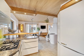 Een moderne keuken met een houten plafond, een ingebouwde kookplaat en een witte koelkast.