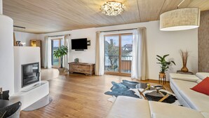 Una sala de estar moderna con televisión de pantalla plana, piso de madera, un sofá, una mesa de centro y una araña.