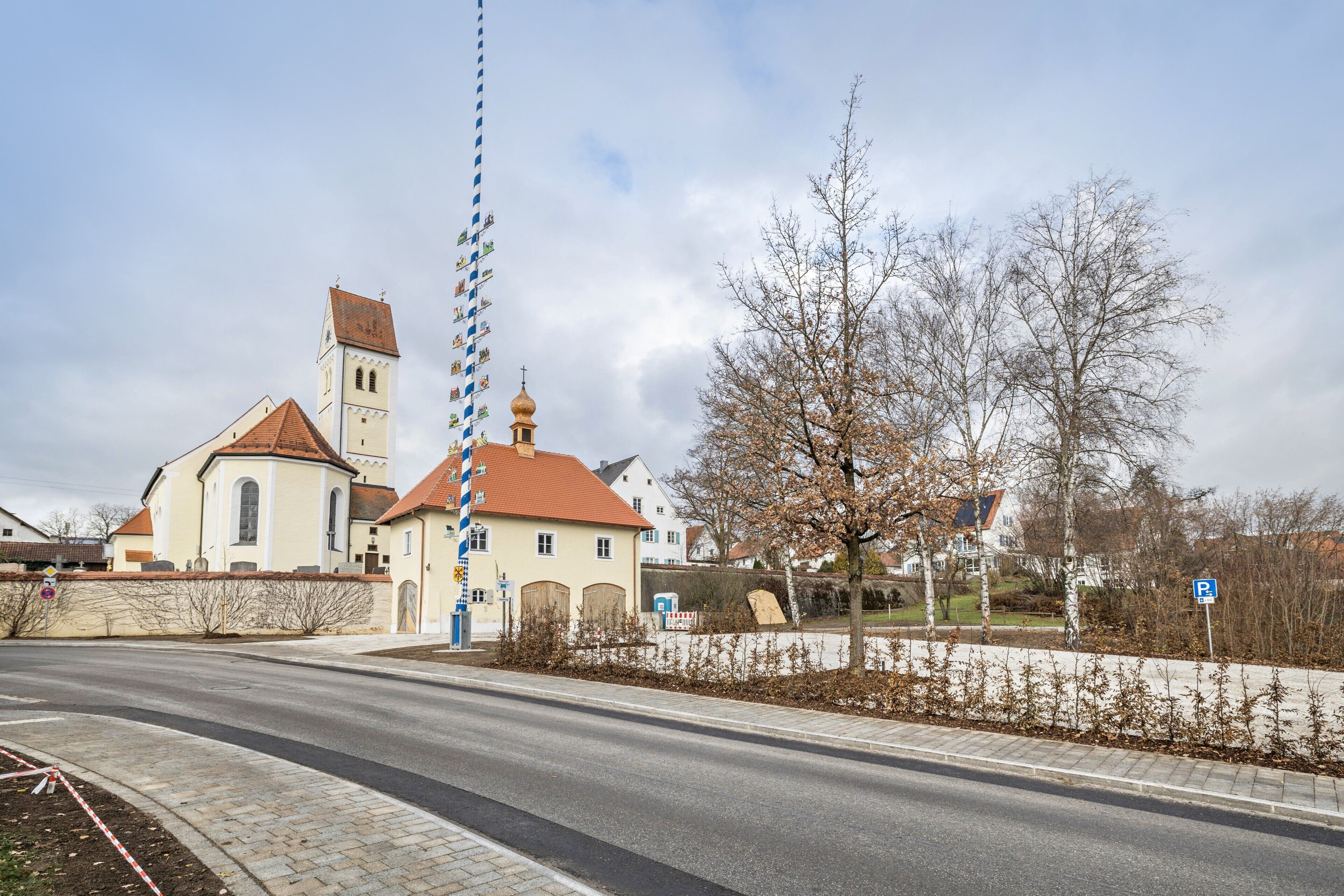 Una iglesia con un alto campanario, una calle pavimentada y una señal de estacionamiento.