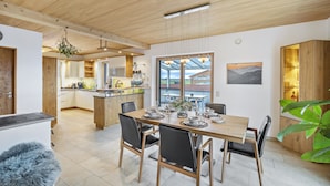 Una cocina moderna con armarios de madera, una zona de comedor con una mesa grande y vistas a través del ventanal.