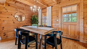 Un interior de fusta amb taula de dinar, cadira, lampadari, mirall i porta amb finestra.