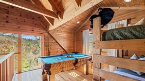 Una cabana de fusta amb billar, lliteres i vistes al bosc.