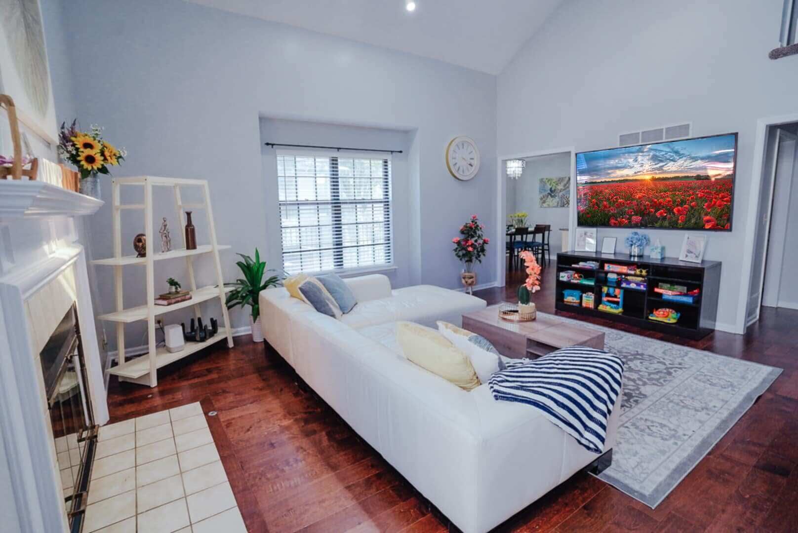 A modern living room with a white sofa, a fireplace, a television, and a large window.