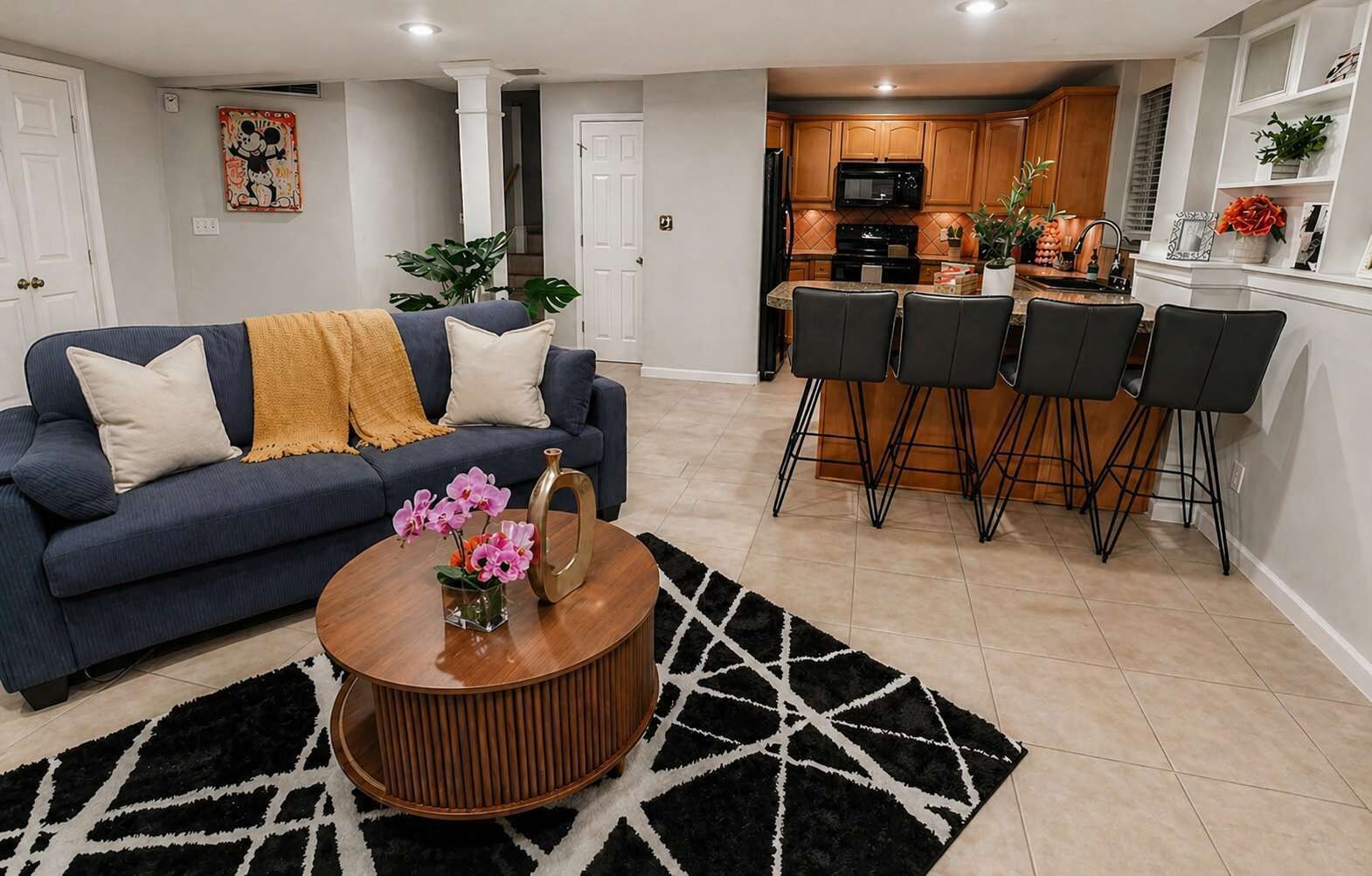 Una sala de estar con sofá, una mesa de centro y sillas, una cocina con muebles de madera y un comedor con taburetes de bar.