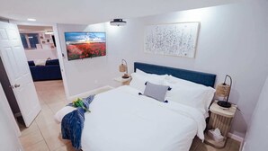 A hotel room with a bed, a TV, a painting, and a view of the outside.