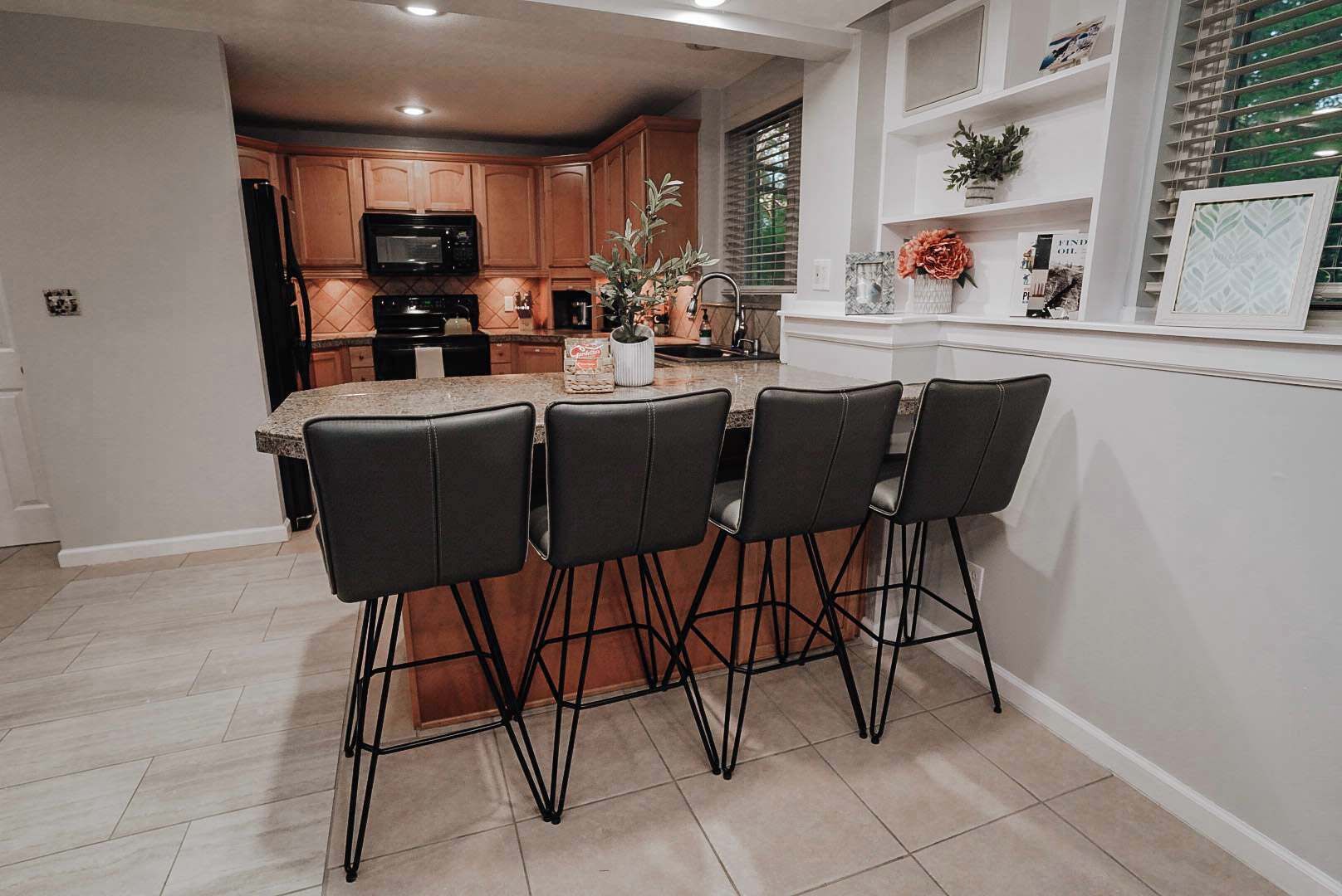 A kitchen with wooden cabinets, a microwave, and a sink. There are four black chairs around a table with a vase and a plant.