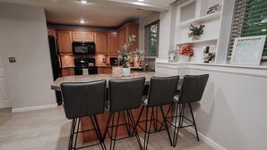 A kitchen with wooden cabinets, a microwave, and a sink. There are four black chairs around a table with a vase and a plant.