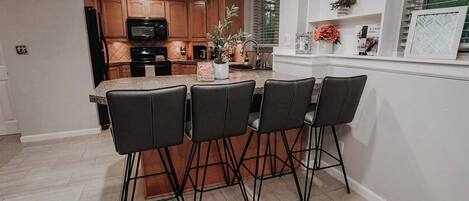 A kitchen with wooden cabinets, a microwave, and a sink. There are four black chairs around a table with a vase and a plant.