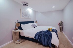 A modern bedroom with a bed, bedside tables, a wall-mounted artwork, and a vase with flowers.