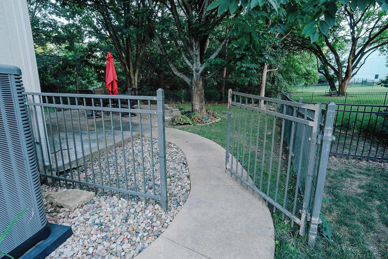 A gated pathway leading to a building, surrounded by trees and a grassy area.