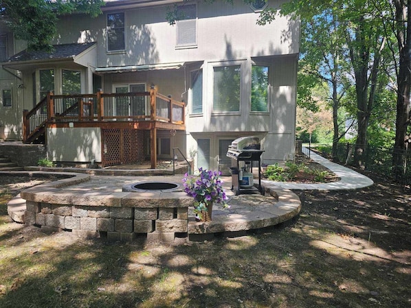 A two-story house with a wooden deck, a stone fire pit, and a landscaped garden.