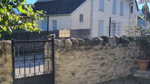 A stone wall with a metal gate, a potted plant, and a building in the background.