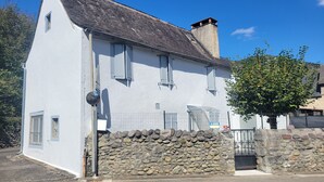 A white building with a stone wall entrance, a metal gate, and a blue sign reading "A LOUER".