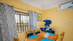 A dining area with a round wooden table, blue upholstered chairs, and a vase of blue flowers. - Bethel Suites Hotel (Accra)