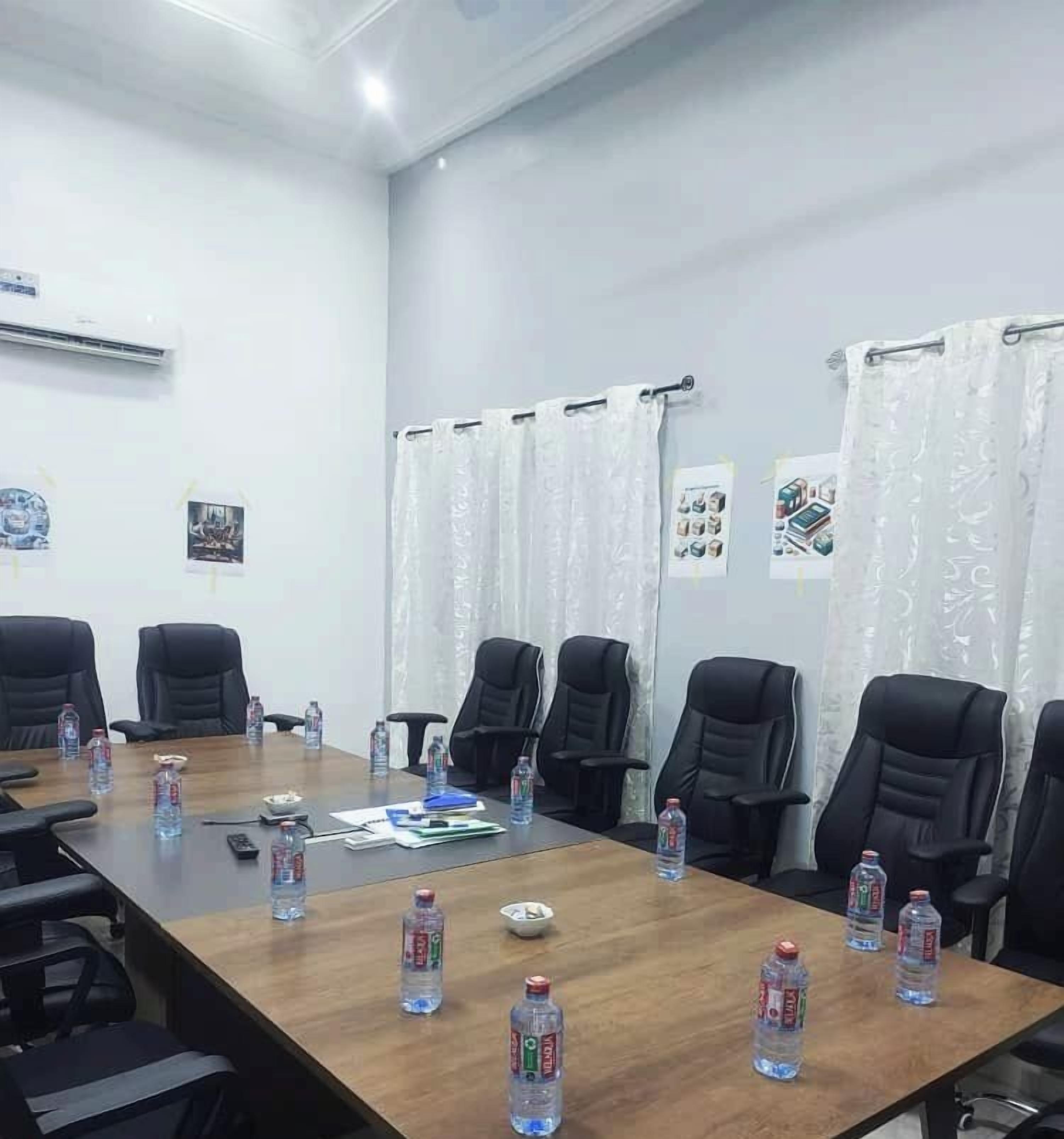 Un salón de conferencias con una larga mesa de madera, sillas negras y botellas de agua.