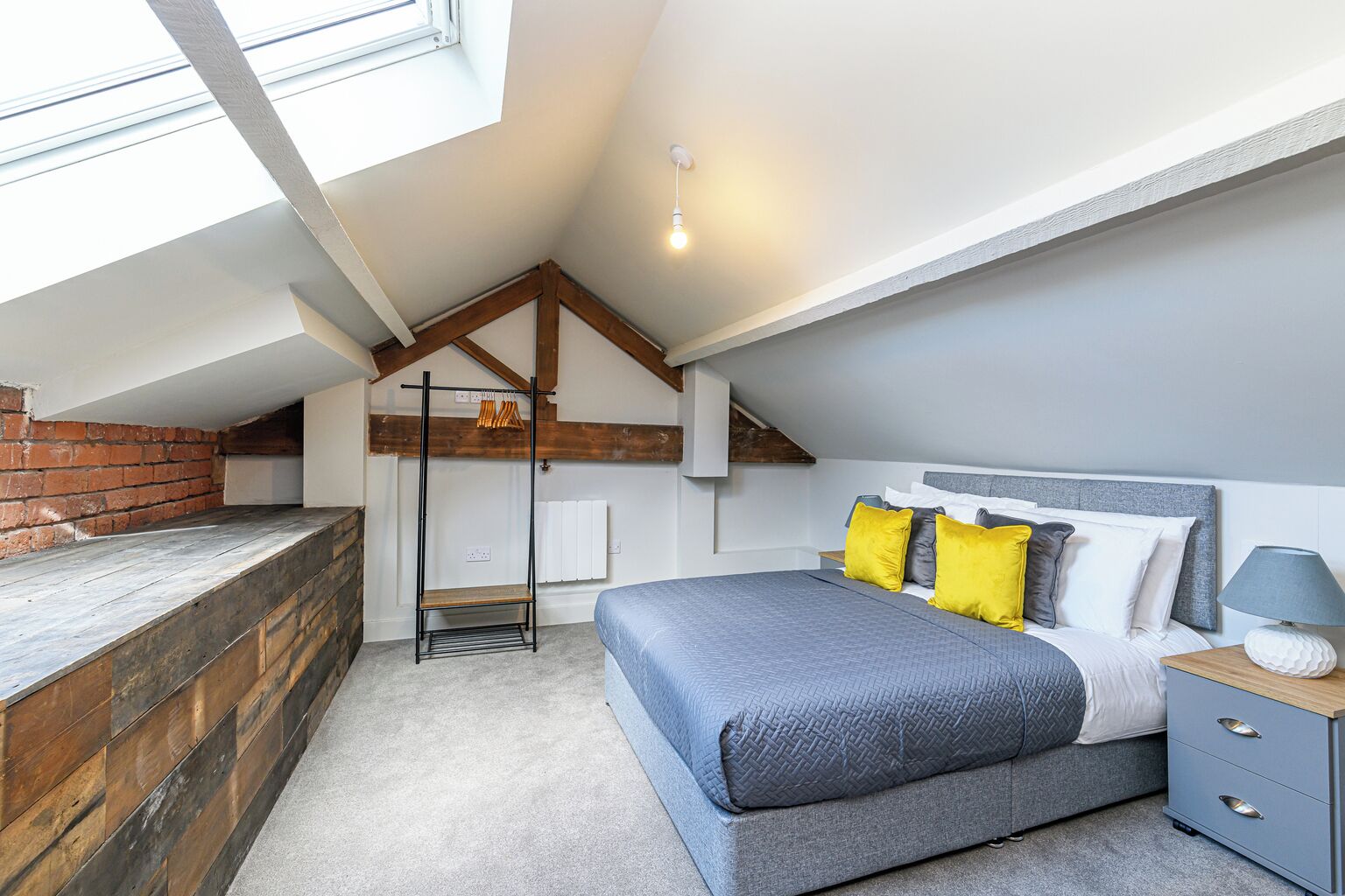 Ein Schlafzimmer mit schrägen Wänden, einem Bett mit vielen Kissen, einem Nachttisch und einem Hängesessel.