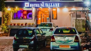Ein mehrstöckiges Hotel mit einem Schild, auf dem "HOTEL KRISHNA WALLABY" steht. Vor dem Gebäude sind Autos geparkt und das Hotel besitzt mehrere Balkone mit Beleuchtung.