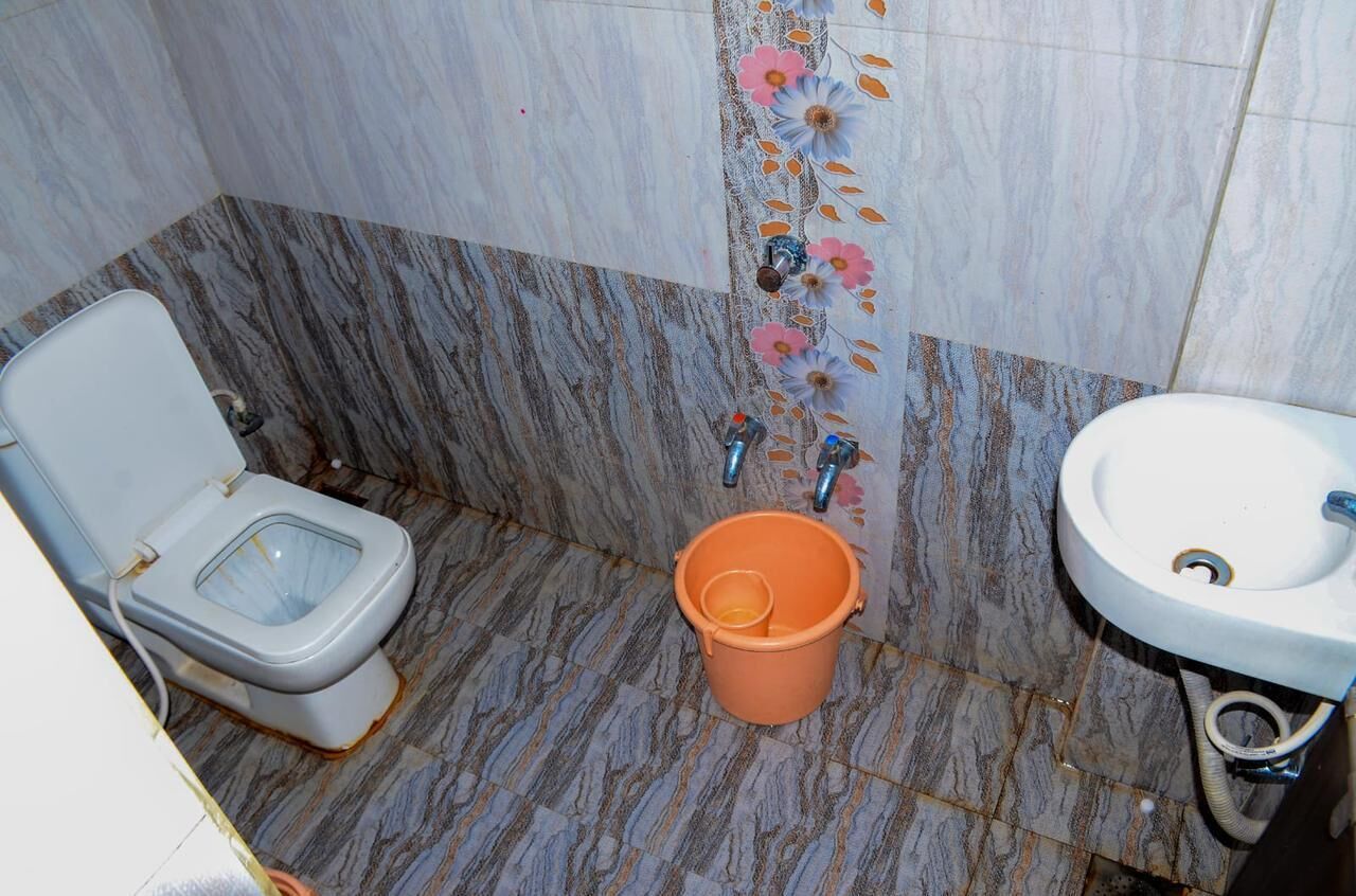 A bathroom with a toilet, a sink, and a bucket on the floor.