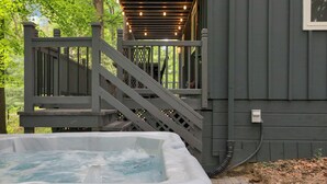 A hot tub adjacent to a wooden deck with a staircase leading to a covered area. - The Roosevelt - Hot Tub, Outdoor games & Walk-to Lake (Rockbridge)