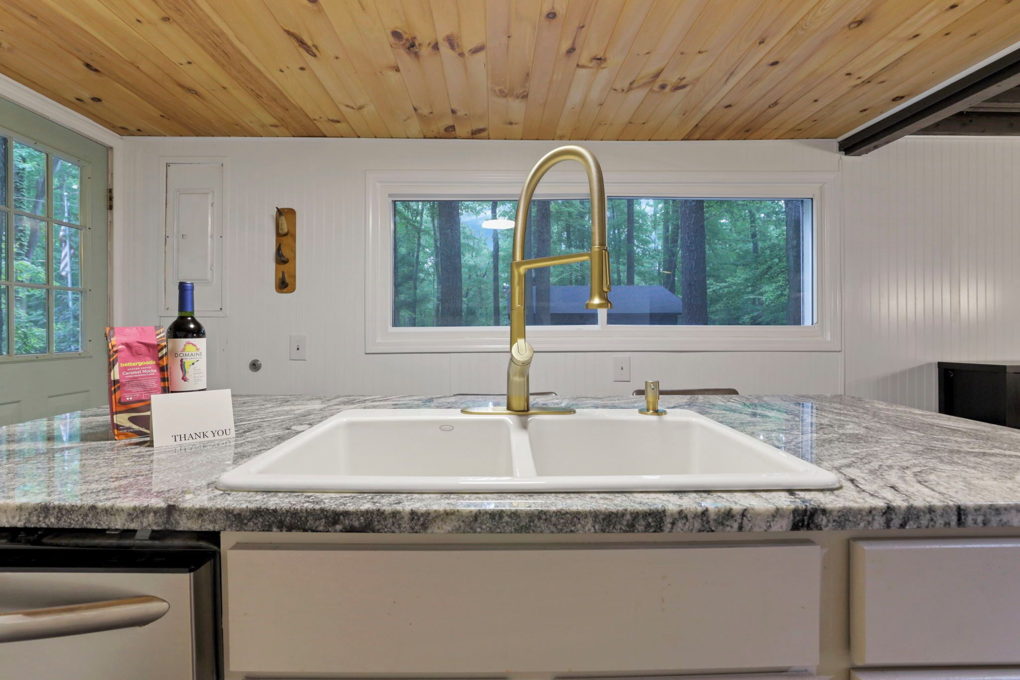 A kitchen with a granite countertop, a gold faucet, a wine bottle, and a thank you card.