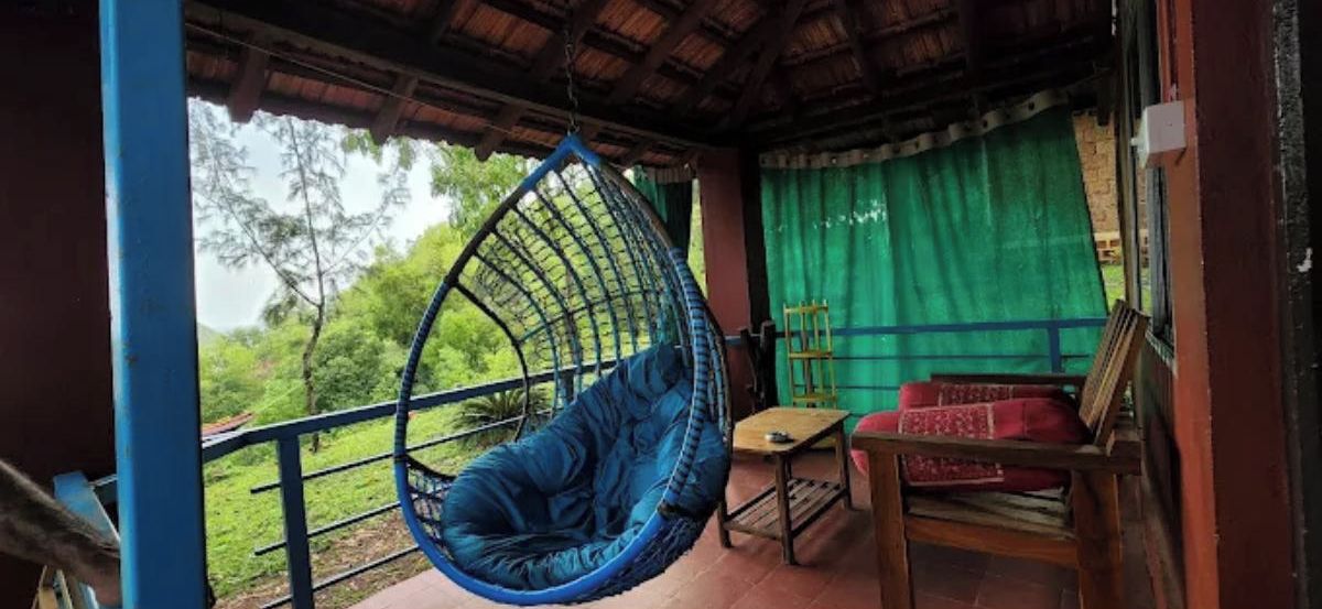 A room with a hanging chair, a small table, and a red sofa.