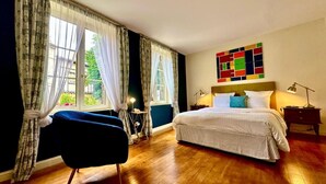 A bedroom with a large bed, a chair, a desk, and a colorful abstract painting on the wall. - Le Logis Plantagenêt (Bergerac)