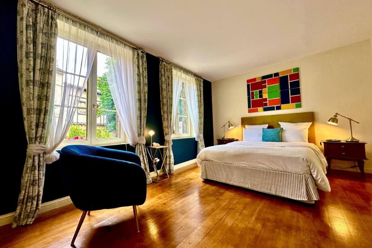 Ein Schlafzimmer mit einem großen Bett, einem Sessel, einem Schreibtisch und einem farbenfrohen abstrakten Gemälde an der Wand.