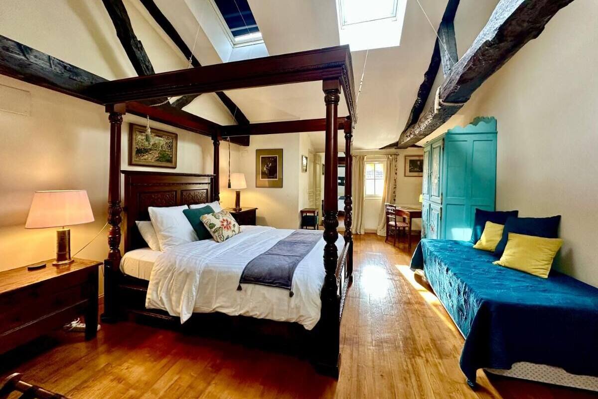 Ein traditionelles Himmelbett mit Baldachin, ein getrenntes Schlafsofa und ein Schreibtisch mit Stuhl in einem Zimmer mit Holzboden und freiliegenden Holzbalken.