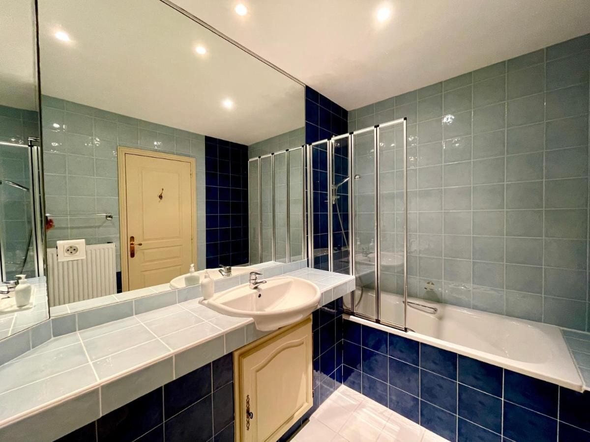 Une salle de bain avec un grand miroir, un lavabo, un espace douche et des murs recouverts de carreaux bleus.