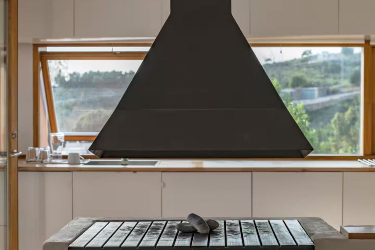 A kitchen with a large window, a wooden table, and a black range hood.