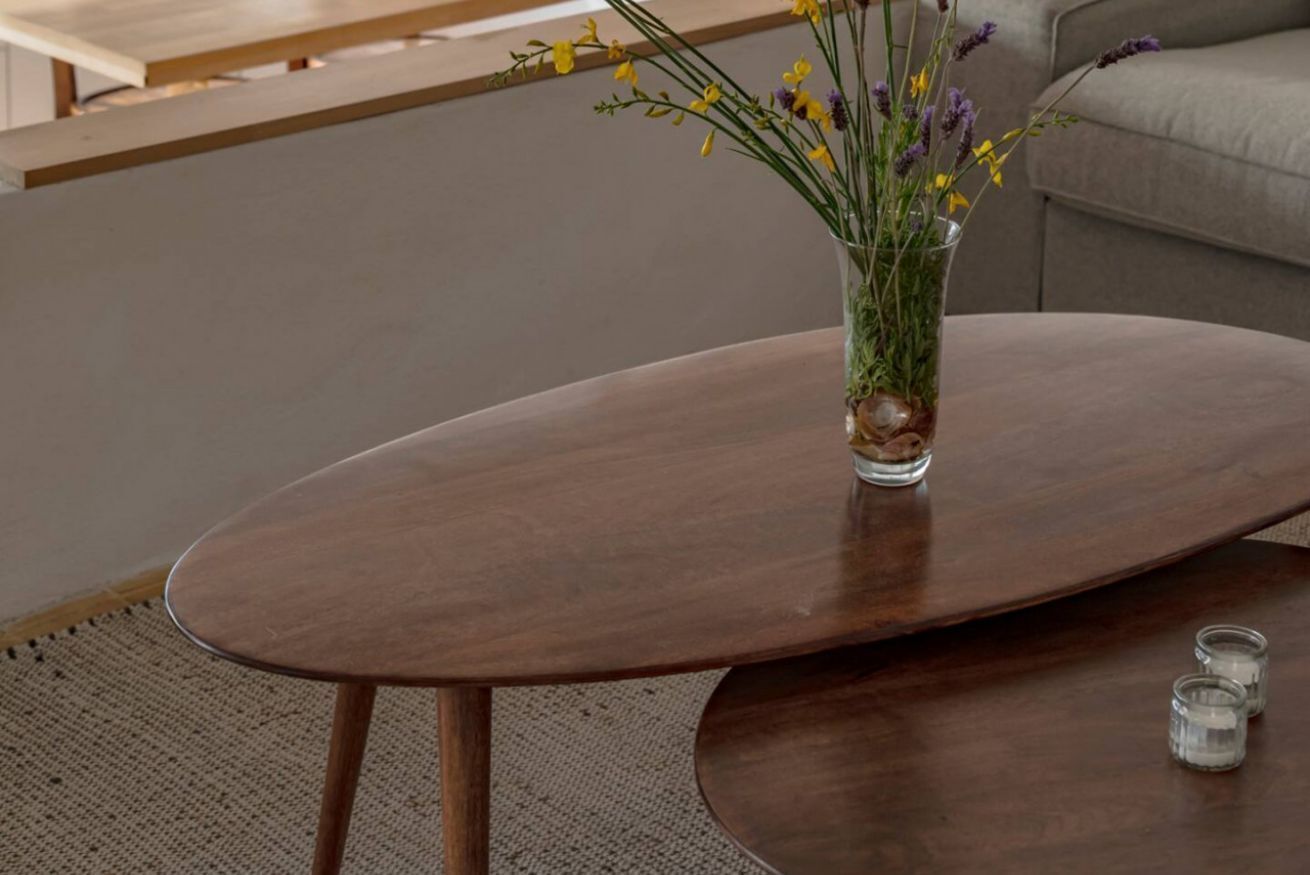 A round wooden table with a glass vase containing flowers.