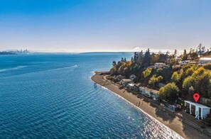 An aerial view of a coastal area with a beach, houses, and a city skyline in the distance.