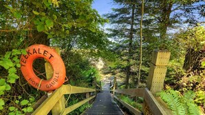 A wooden staircase leading uphill, surrounded by dense greenery and a lifebuoy labeled 'TEEKALET FOR GAMBLE' on the left. - Poulsbo's Waterfront Lodge · Puzzle Point (Poulsbo)