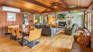 A cozy living room with a fireplace, wooden furniture, and large windows. - Poulsbo's Waterfront Lodge · Puzzle Point (Poulsbo)