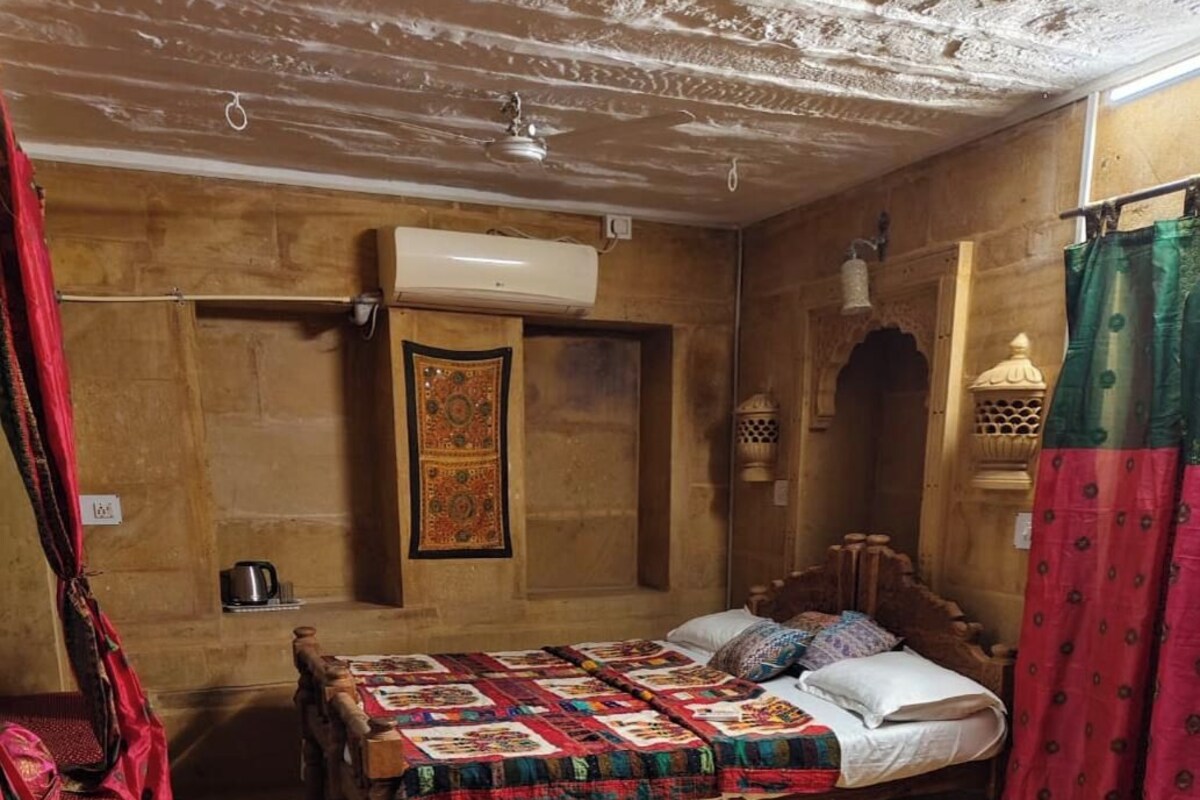 Une chambre traditionnelle avec un lit en bois, un vêtement rouge suspendu, un tapis  à motifs et une décoration murale.