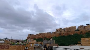 A view of a cityscape with a prominent rocky hill in the background and a cloudy sky. - Hotel Choti Haveli (Jaisalmer)