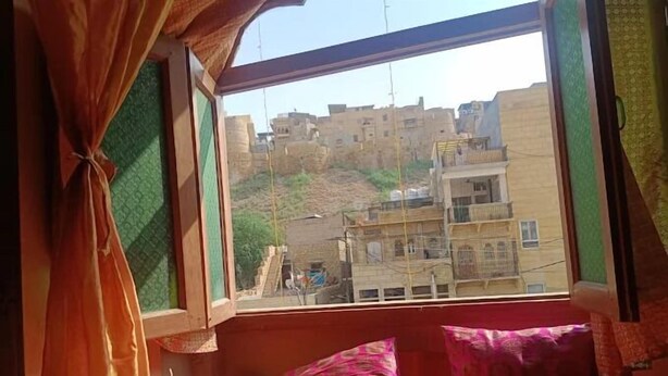 A room with a window overlooking a hillside with buildings. There are two pillows on the window sill. - Hotel Choti Haveli (Jaisalmer)