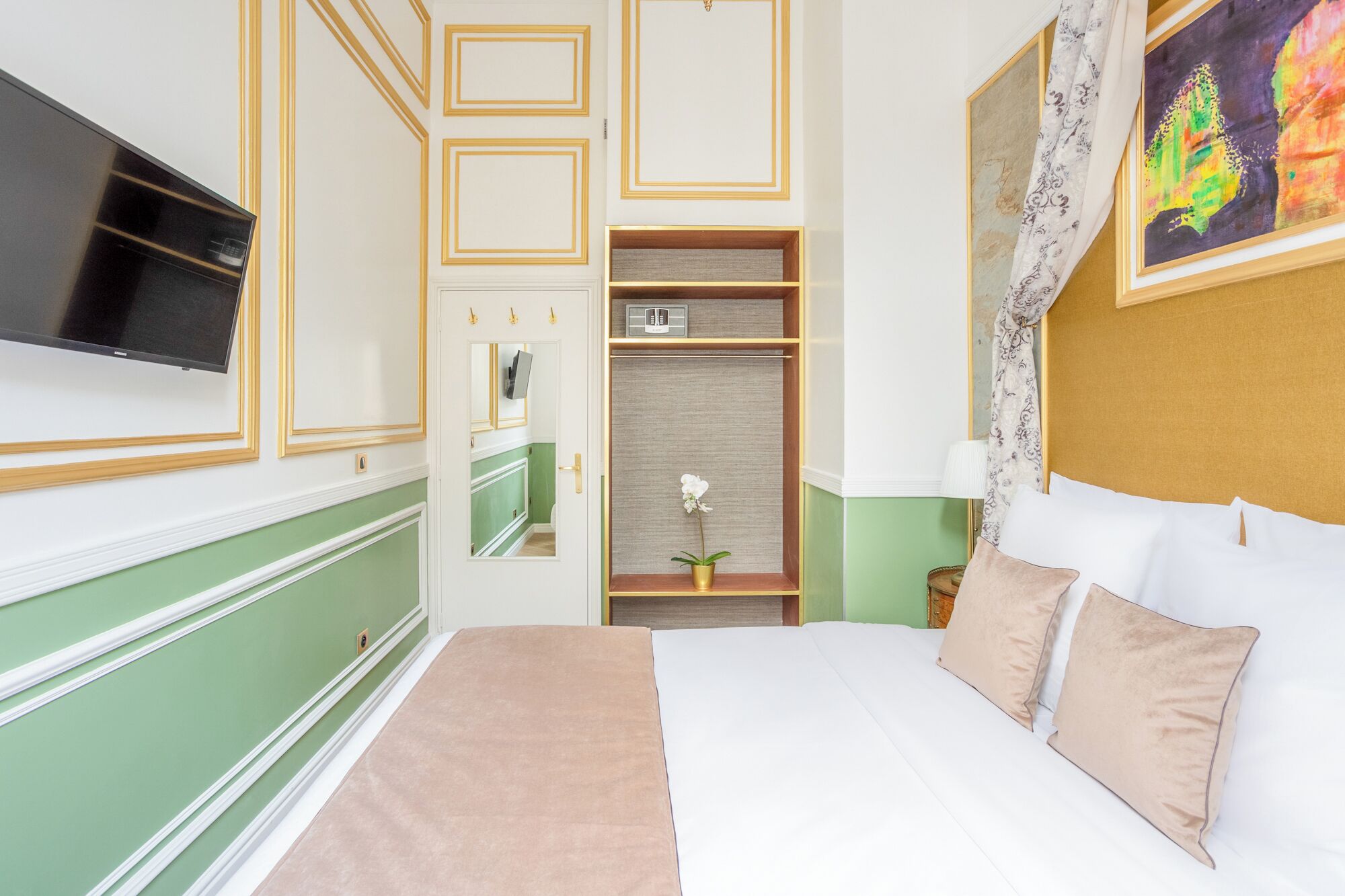 A hotel room with a bed, a television, a wardrobe, and a painting on the wall.