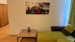 Una sala de estar con un sofá, una mesa de centro con una planta y un cuadro de un coche y una persona.
