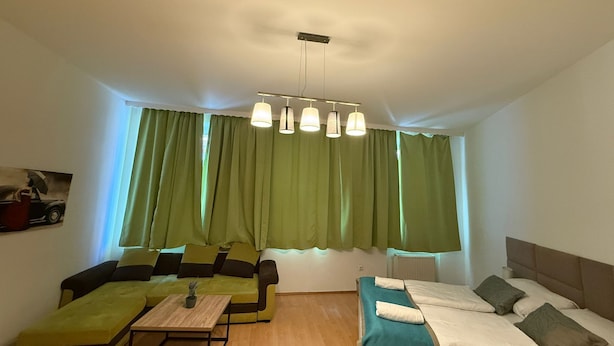 Una habitación con sofá, cama, una mesita y ventana con cortinas verdes.
