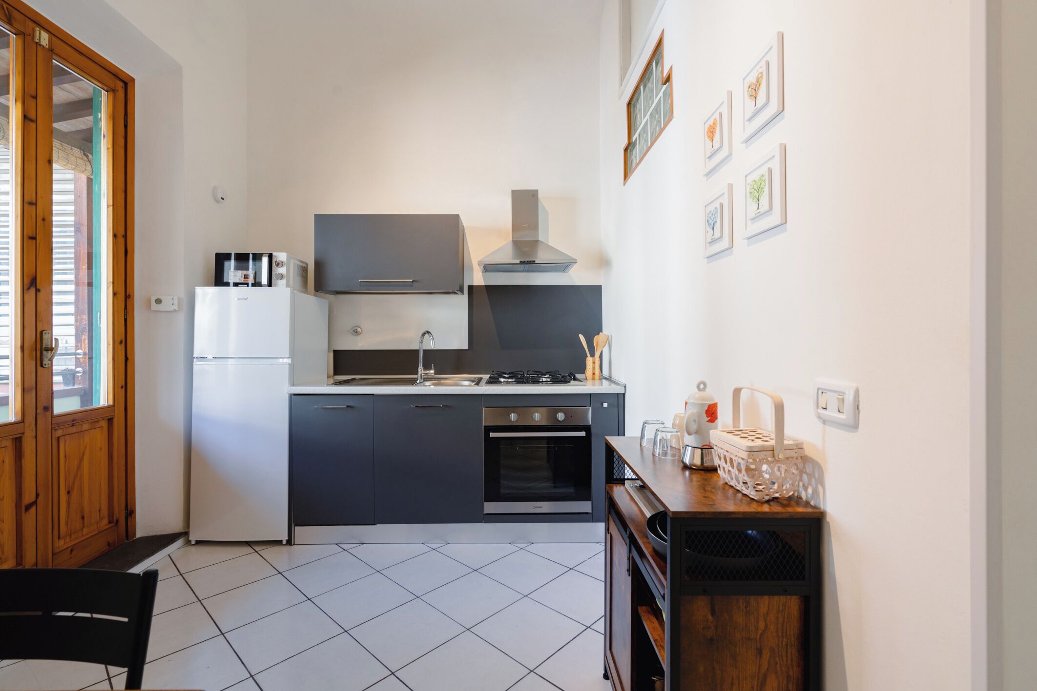 A compact kitchen with a refrigerator, stove, oven, and microwave. There is a wooden door and a dining area with a chair.