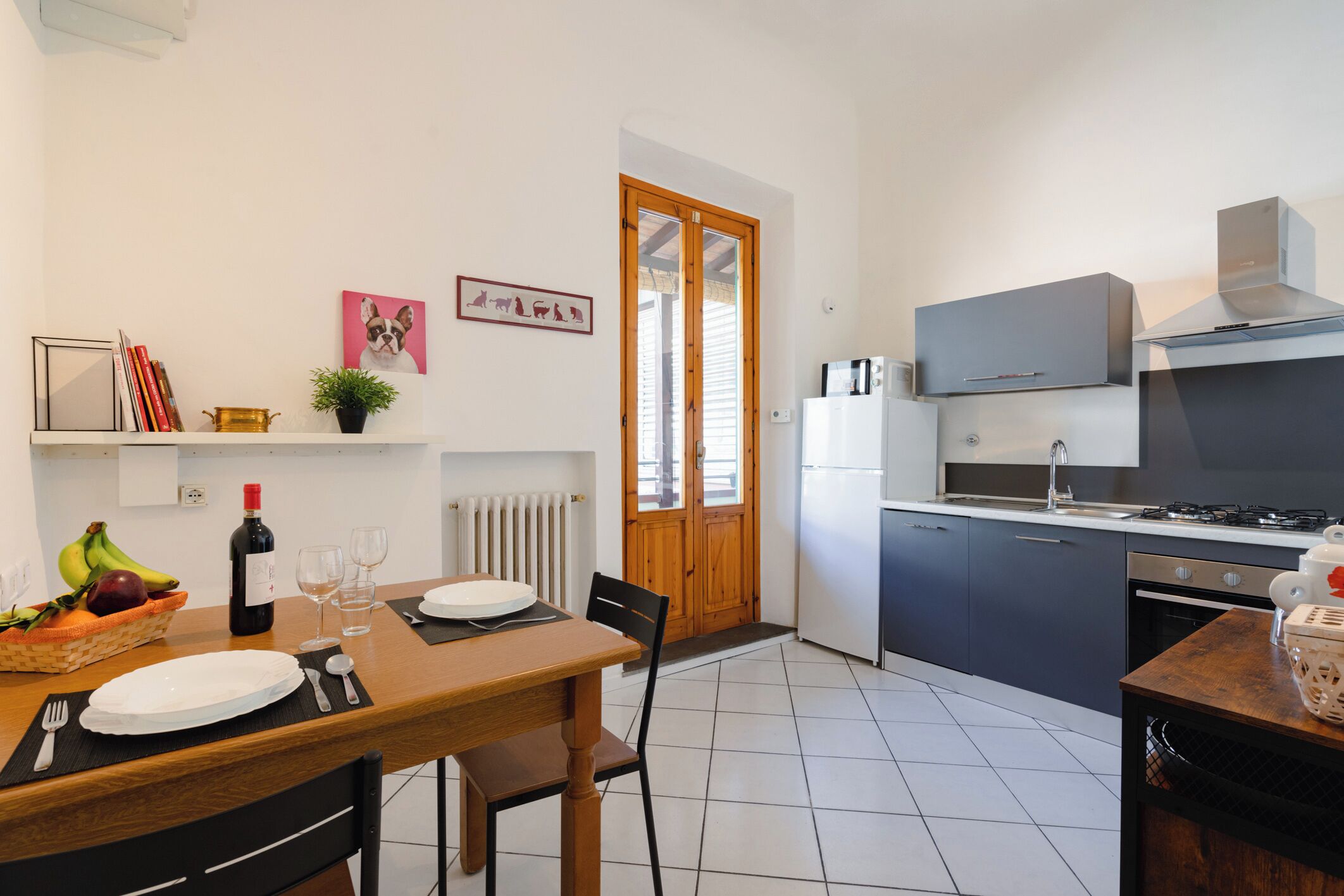 A modern kitchen with a dining area, featuring a stove, refrigerator, and a wooden dining table set for two.